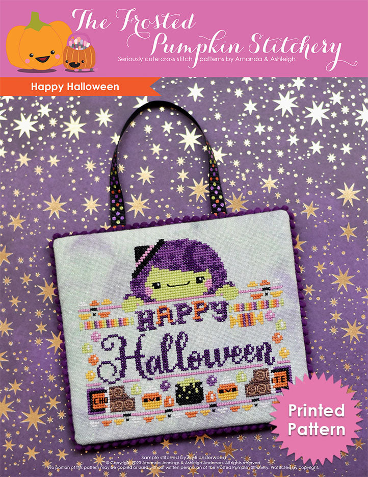 A cross stitched sign rests on a piece of purple scrapbook paper with metallic gold stars. The sign features a green skinned witch with purple hair. The text reads "Happy Halloween" and it is surrounded by candy.