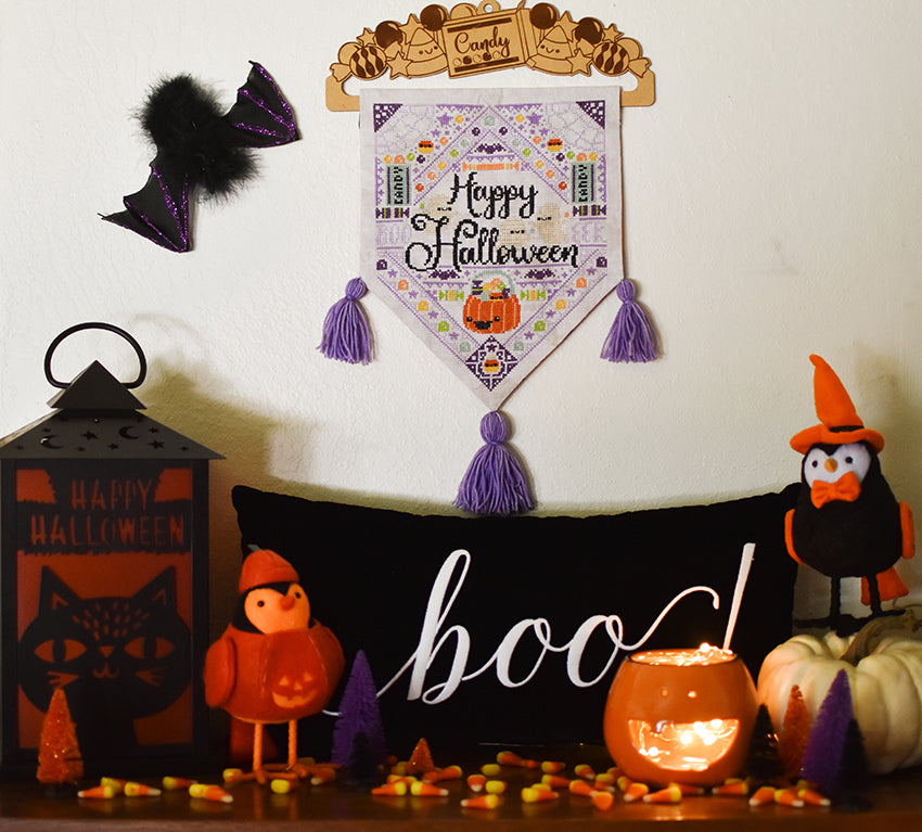 Jack's Halloween Dream counted cross stitch pattern hanging in our home. Pillow with text that says "boo" on a pillow, a lantern that says "happy halloween" and candy corn.