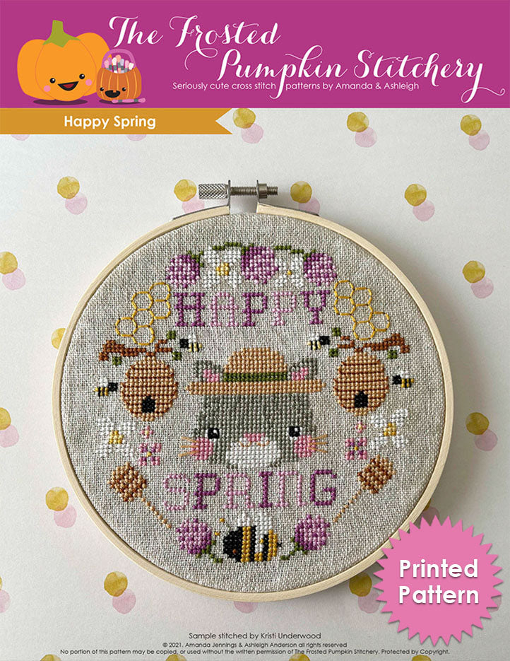 Happy Spring cross stitch pattern. Image of an embroidery hoop with a cat who looks grumpy with stripes. She's surrounded by thistles, honey wands, bees. Printed Pattern.