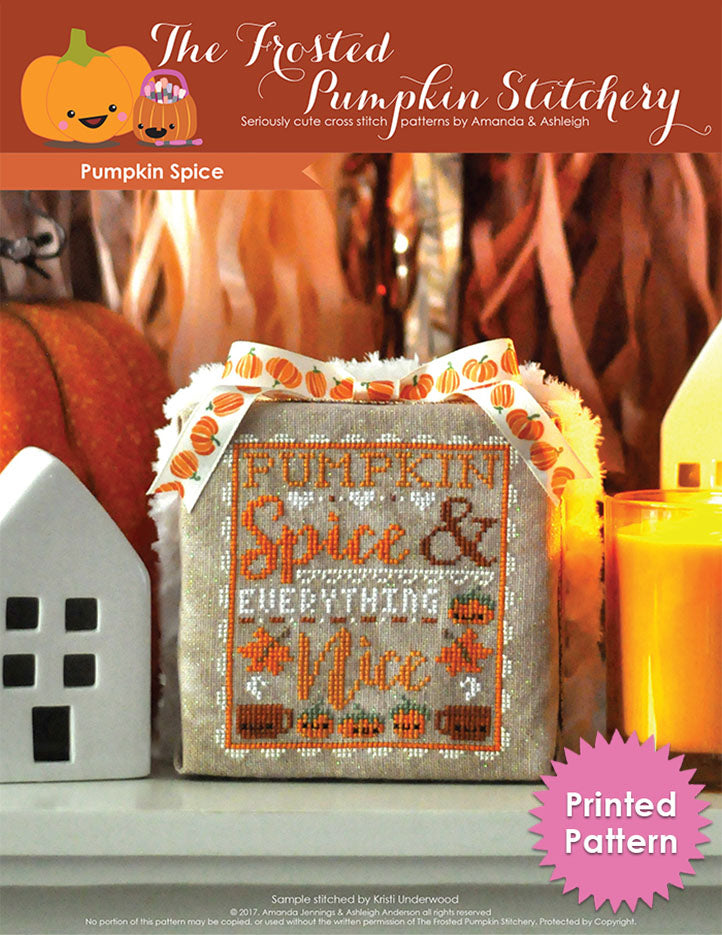Pumpkin Spice counted cross stitch pattern. Finished as a foam cube it's resting on a white mantle surrounded by a ceramic house and candle. Text reads "Pumpkin Spice and Everything Nice". Printed Pattern.
