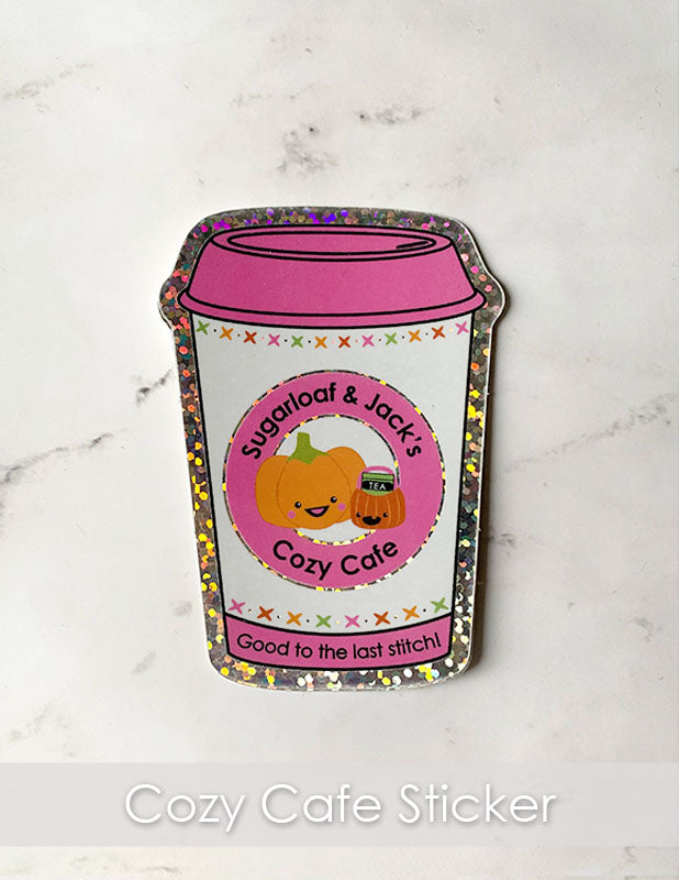 Glitter coffee cup silhouette sticker with Sugarloaf and Jack pumpkin with a pink lid and logo. Text reads "Sugarloaf & Jack's Cozy Cafe" "Good to the last stitch".