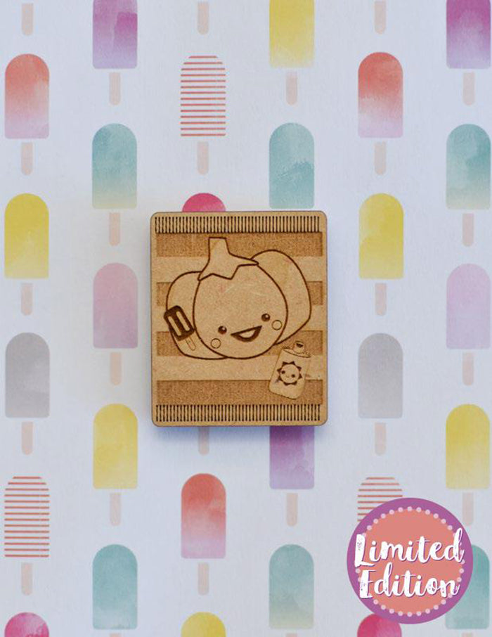 Image of a wooden needleminder with a Pumpkin on a beach towel with suntan lotion holding a popsicle. 