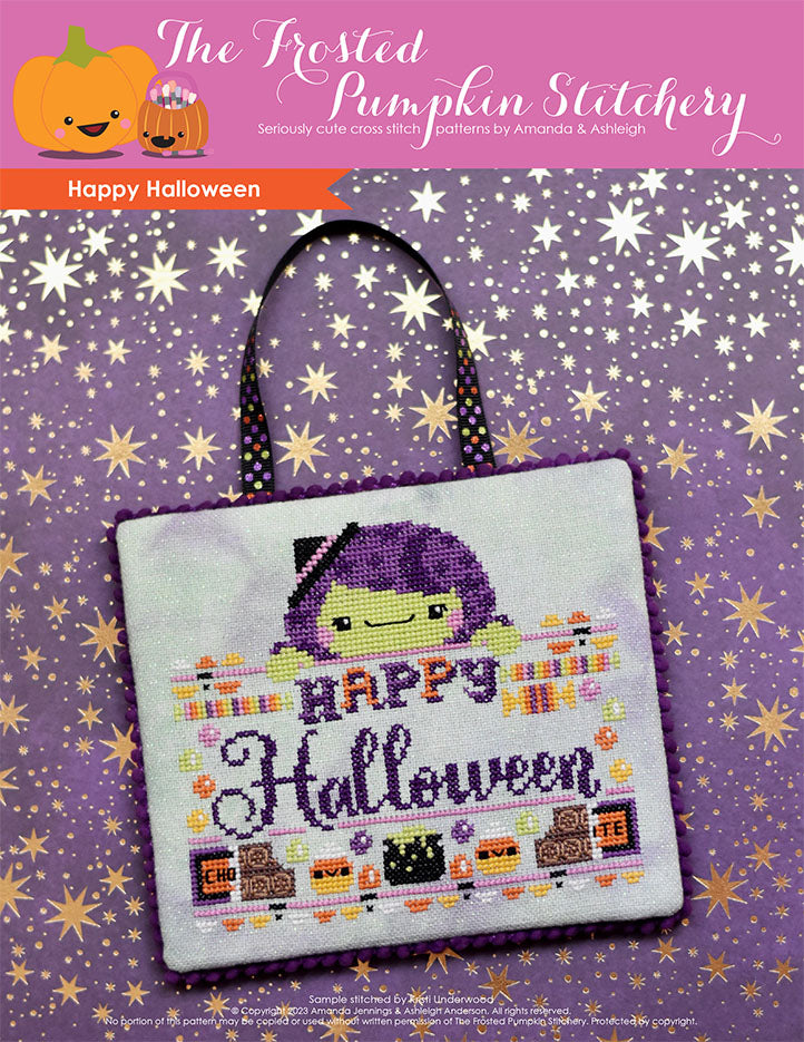 A cross stitched sign rests on a piece of purple scrapbook paper with metallic gold stars. The sign features a green skinned witch with purple hair. The text reads "Happy Halloween" and it is surrounded by candy of all different kinds.