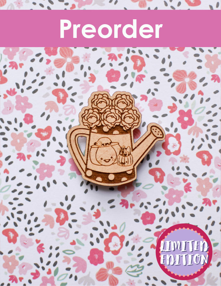 Wooden needleminder of a watering can with flowers on a floral patterned background, labeled 'Preorder Limited Edition'.
