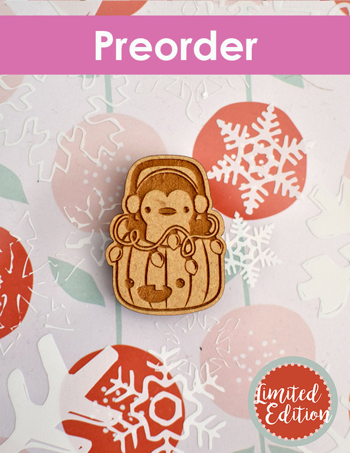 Wooden needleminder of a penguin in Jack's bucket on a festive background with snowflakes.