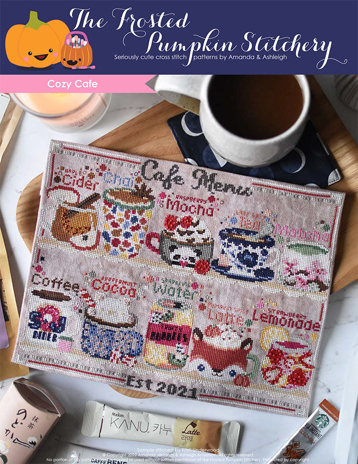 Cozy Cafe Club Pattern Cover. Cover image features a stitched raspberry mocha, matcha, Earl Grey tea, strawberry lemonade, sparkling water, coffee, apple cider, pumpkin spice latte, chai and peppermint hot cocoa sitting on a shelf and the words "Cafe Menu" above them. The stitched project has a cup of coffee and different flavored tea and coffee packets scattered around it.