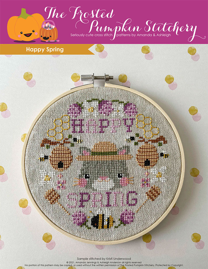 Happy Spring cross stitch pattern. Image of an embroidery hoop with a cat who looks grumpy with stripes. She's surrounded by thistles, honey wands, bees.