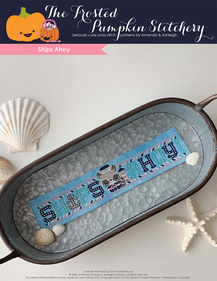 Ships Ahoy Cross Stitch Pattern image of a silver rustic tray with a finished cross stitch pattern of Reece the Raccoon inside of it. The piece is blue with navy blue, aqua and pink lettering spelling out Ships Ahoy. Reece stands in the center dressed as a sailor.