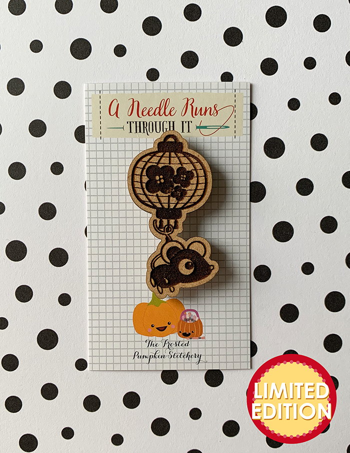 Image of a wooden needleminder with little rat hanging from a Chinese paper lantern. The lantern has plum blossoms on it.