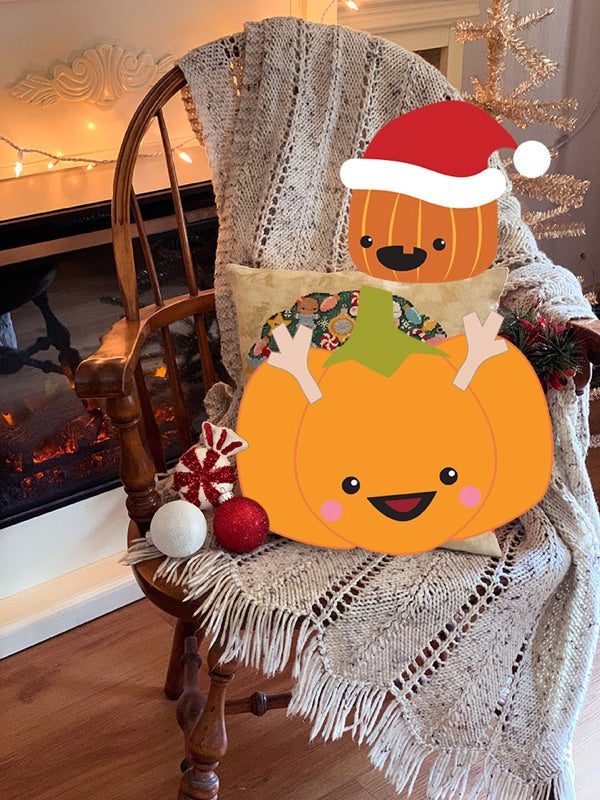 Sugarloaf the Pumpkin is dressed as a reindeer and he's sitting on a chair with a knit afghan. Jack the Pumpkin is wearing a Santa hat and is perched on the Christmas Wreath sample pillow. The background is a fireplace and a silver tinsel tree.