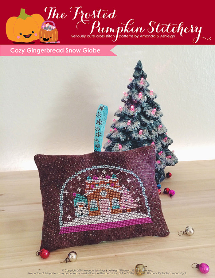 Cozy Gingerbread Snow Globe counted cross stitch pattern. A snowglobe with a snowman, gingerbread house and pink tree.