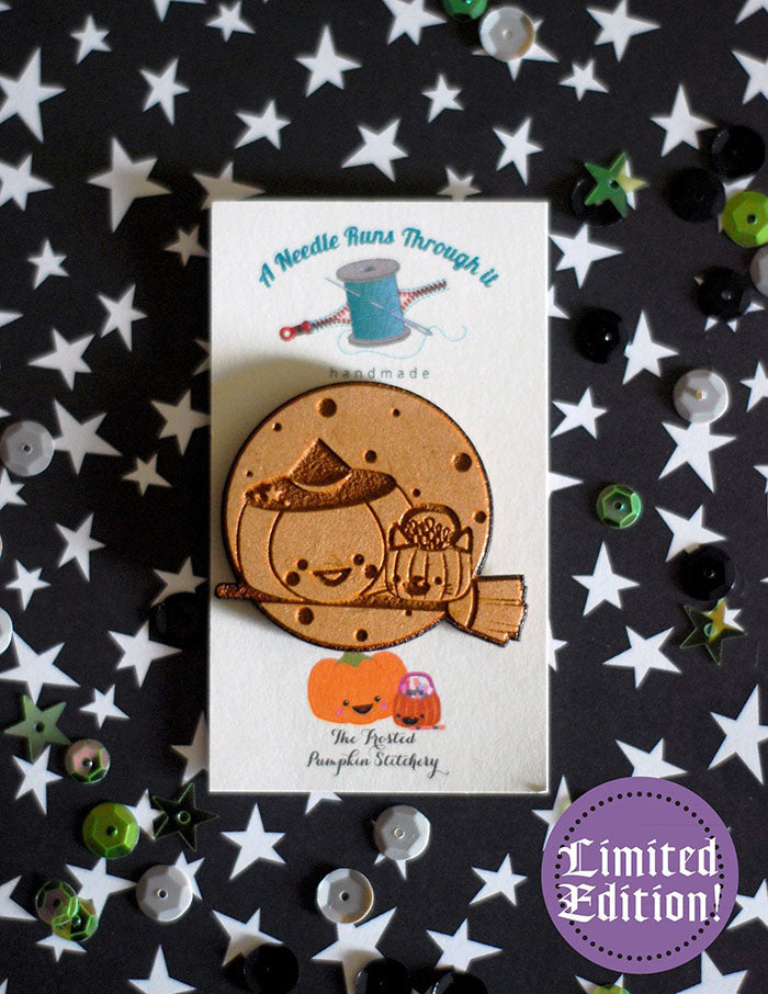 Image of a wooden needleminder with two pumpkins riding a broom flying over the moon