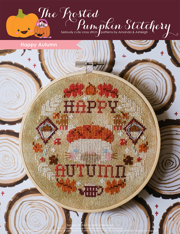 An embroidery hoop with a cream colored cat wearing a beret surrounded by leaves, kites, mittens, wheat, a pumpkin and tea pot and the text "Happy Autumn."
