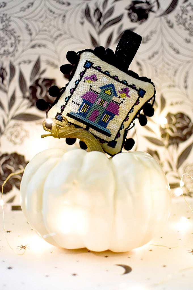 Haunted Birdhouse Halloween counted cross stitch pattern. Ornament placed on top of a white pumpkin.