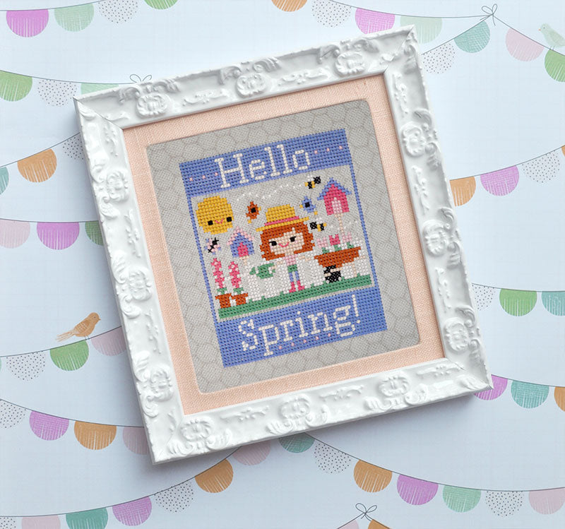 Hello Spring counted cross stitch pattern. A white girl with red hair is gardening. Text reads "Hello Spring". It's framed in a white frame with peach molding.