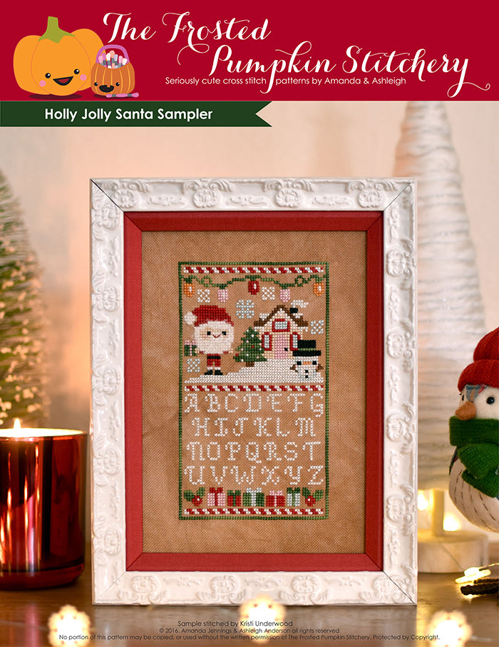 Holly Jolly Sampler counted cross stitch pattern. Christmas pattern with santa, a snowman and a little house above the alphabet. Surrounded by a ceramic house, a fake bird wearing a hat and a bristle tree.