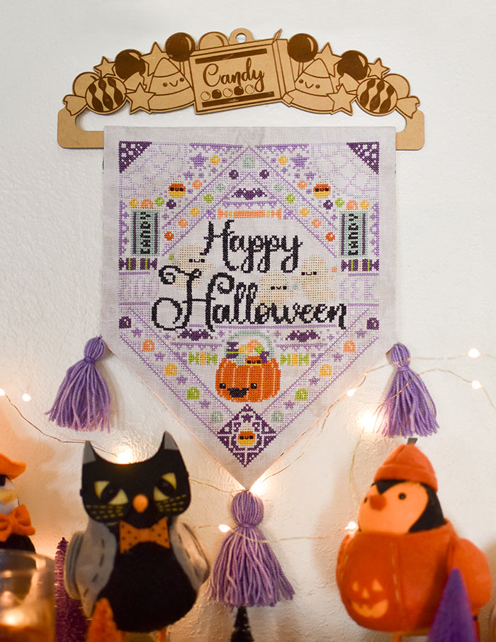 Jacks Halloween Dream counted cross stitch pattern. A hanging banner on a white wall surrounded by twinkle lights and a black and orange birds. Text reads "Happy Halloween".