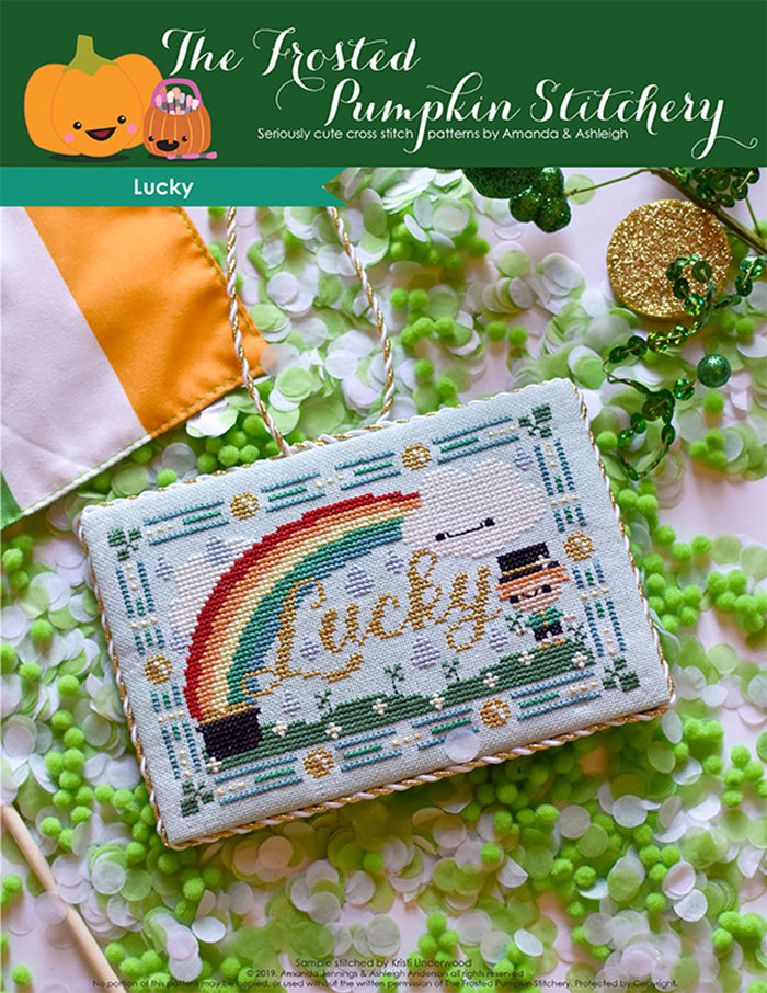 Lucky counted cross stitch pattern. Finished as a flat fold with gold and white trim. Pattern is a rainbow with a pot of gold, a cloud with a face, a leprechaun and grass.