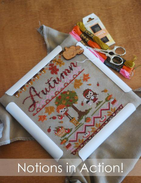 Notions in action! Image of cross stitch project being held in a Q-Snap frame while using a needleminder and surrounded by embroidery floss, a pack of needles and scissors.