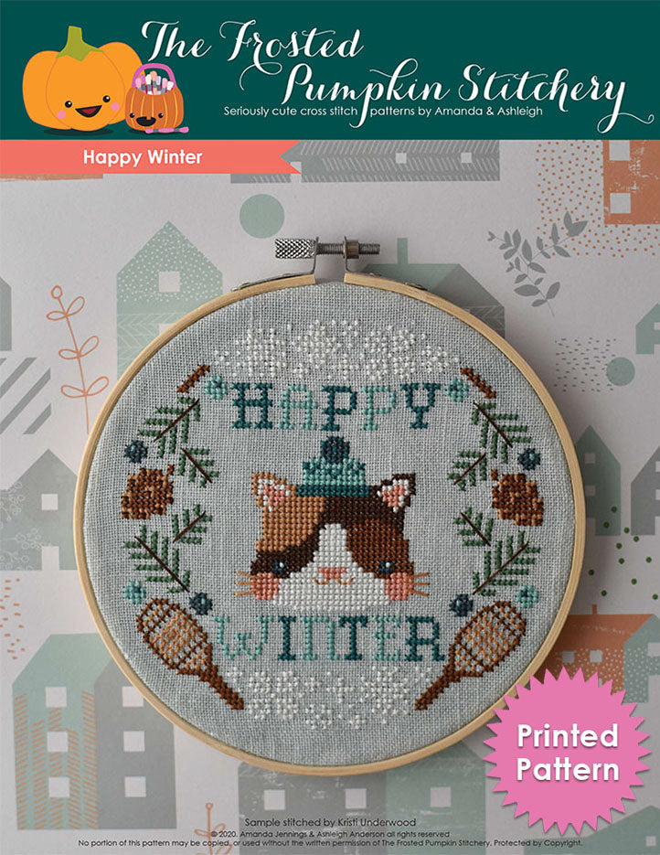 Happy Winter counted cross stitch pattern. This pattern features a cat wearing a winter cap surrounded by the words "Happy Winter," pine boughs, pine cones, snowshoes, snowflakes and juniper berries. Printed Pattern.