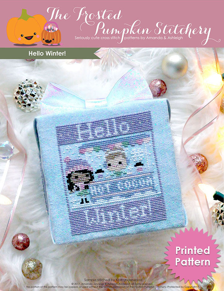 Hello Winter counted cross stitch pattern. A brown skinned girl with long dark hair is having hot cocoa with a white skinned boy with short light brown hair at a hot cocoa stand. Text reads "Hello Winter". Printed Chart.