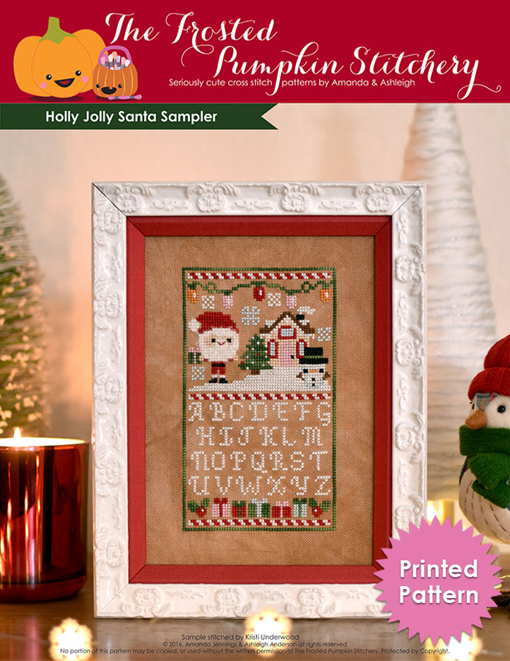 Holly Jolly Sampler counted cross stitch pattern. Christmas pattern with santa, a snowman and a little house above the alphabet. Surrounded by a ceramic house, a fake bird wearing a hat and a bristle tree. Printed Chart.