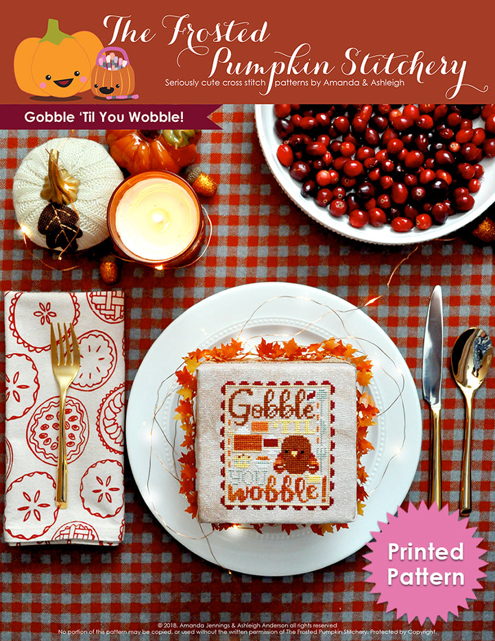 Gobble 'Til You Wobble Thanksgiving counted cross stitch pattern. A finished cross stitch pattern in a plate with place settings and cranberries. Text reads "Gobble Til You Wobble". Printed Pattern.