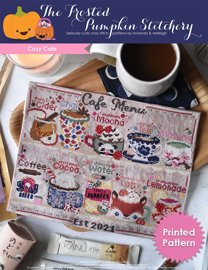 Cozy Cafe Club Pattern Cover. Cover image features a stitched raspberry mocha, matcha, Earl Grey tea, strawberry lemonade, sparkling water, coffee, apple cider, pumpkin spice latte, chai and peppermint hot cocoa sitting on a shelf and the words "Cafe Menu" above them. The stitched project has a cup of coffee and different flavored tea and coffee packets scattered around it.