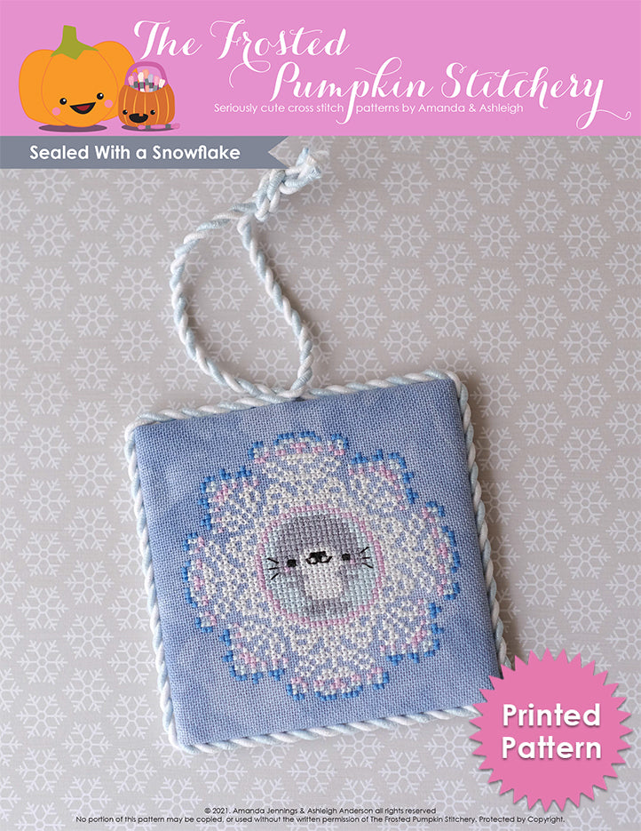Sealed With a Snowflake cross stitch pattern, printed version. A gray seal is in the middle of a white snowflake with pink and blue edges. Stitched on gray fabric.