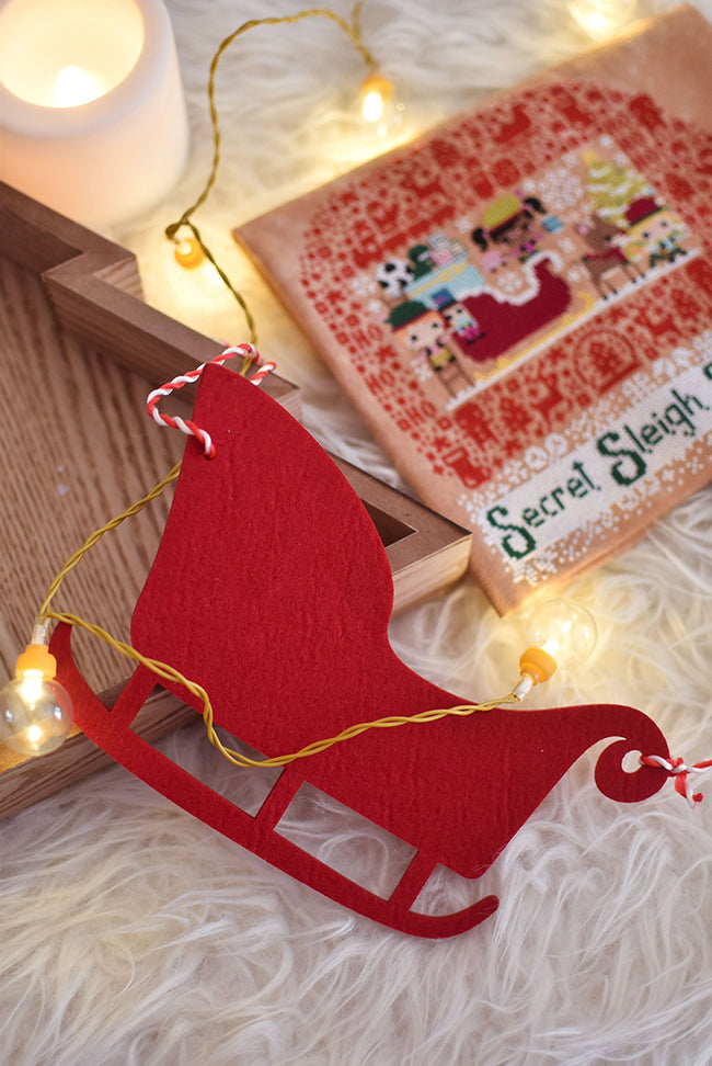 A felt sled on a fake sheep skin rug with candles and Secret Sleigh Society in the background.