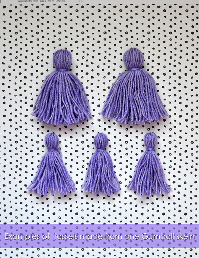 Examples of tassels that can be made from one mini skein of Knitted Wit Gumball yarn. Two large purple tassels and three small tassels.