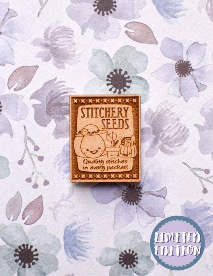 Image of a wooden needleminder with a vintage seed packet. Text reads "quality stitches in every packet".