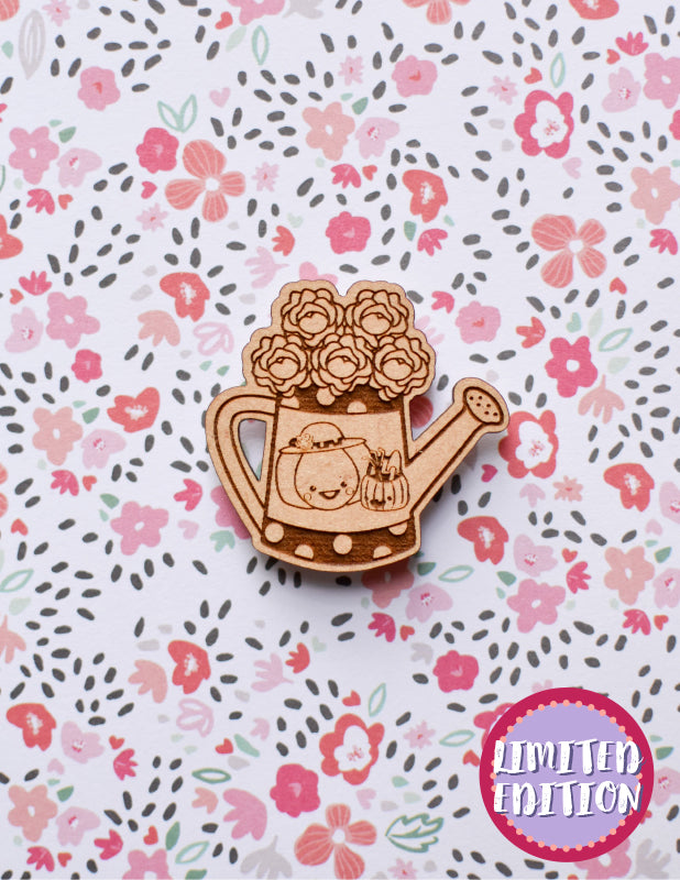 Image of a wooden needleminder with a watering can with flowers in it.