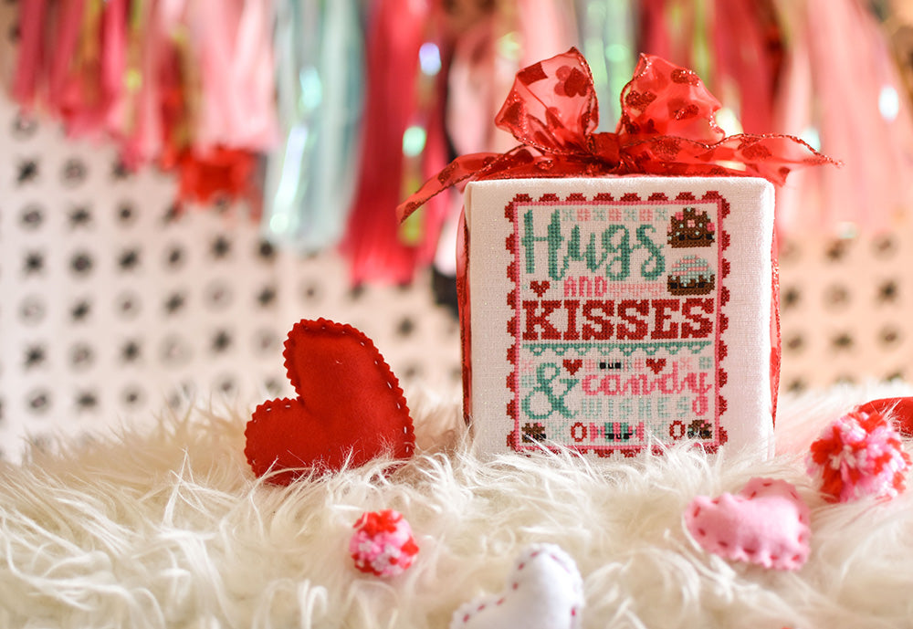Hugs and Kisses counted cross stitch pattern. Valentine's Day cross stitch pattern surrounded by felt hearts. Text reads "Hugs and kisses and candy wishes"